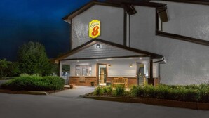 A Super 8 hotel with a well-lit entrance, a bench outside, and a landscaped garden area. - Super 8 by Wyndham Boone (Boone)