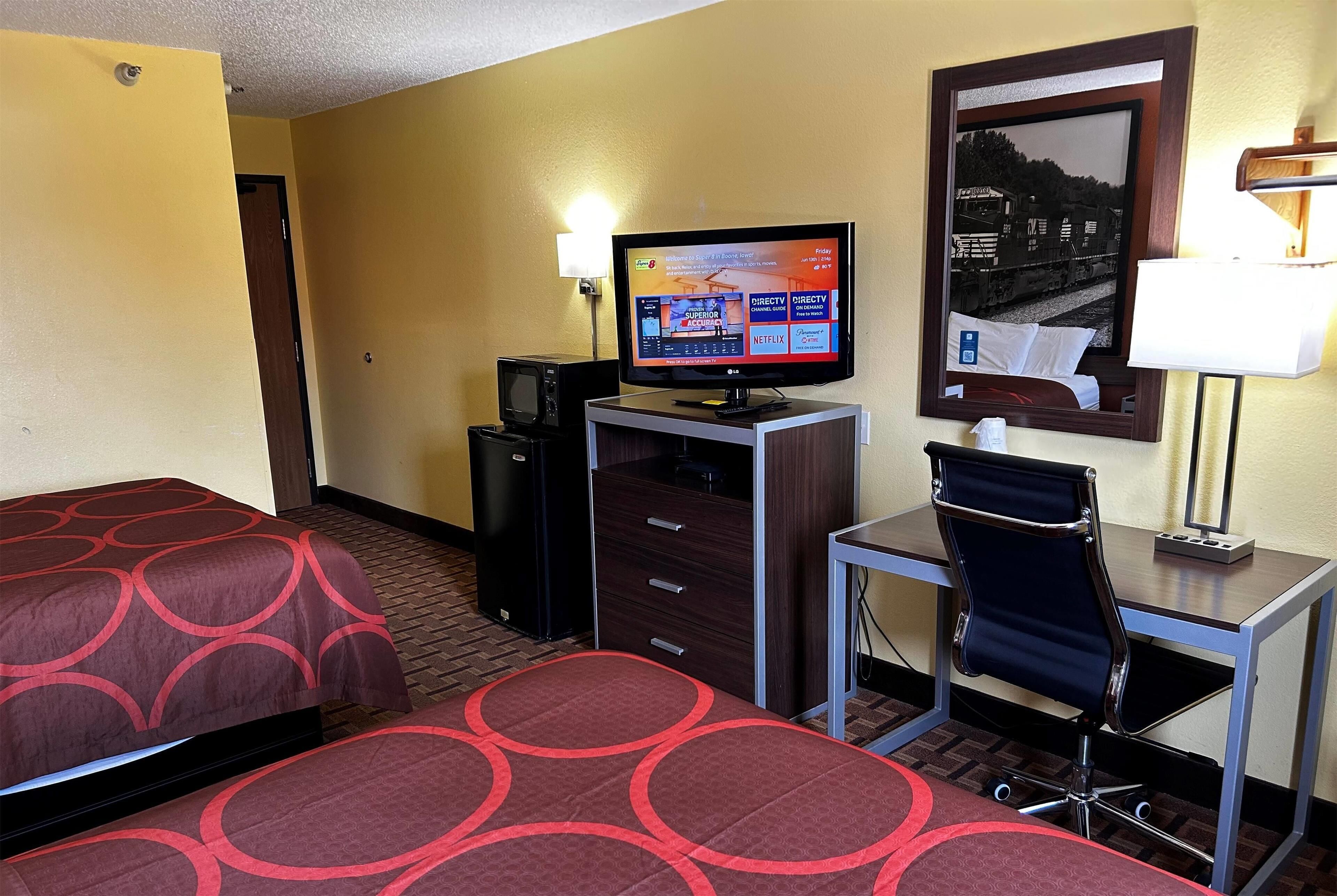 Una habitación de hotel con dos camas, un escritorio, una silla, un televisor y una lámpara de escritorio.
