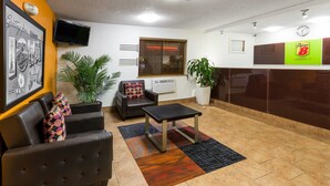 A lobby with a sofa, a small table, a potted plant, a wall-mounted TV, and a reception desk.