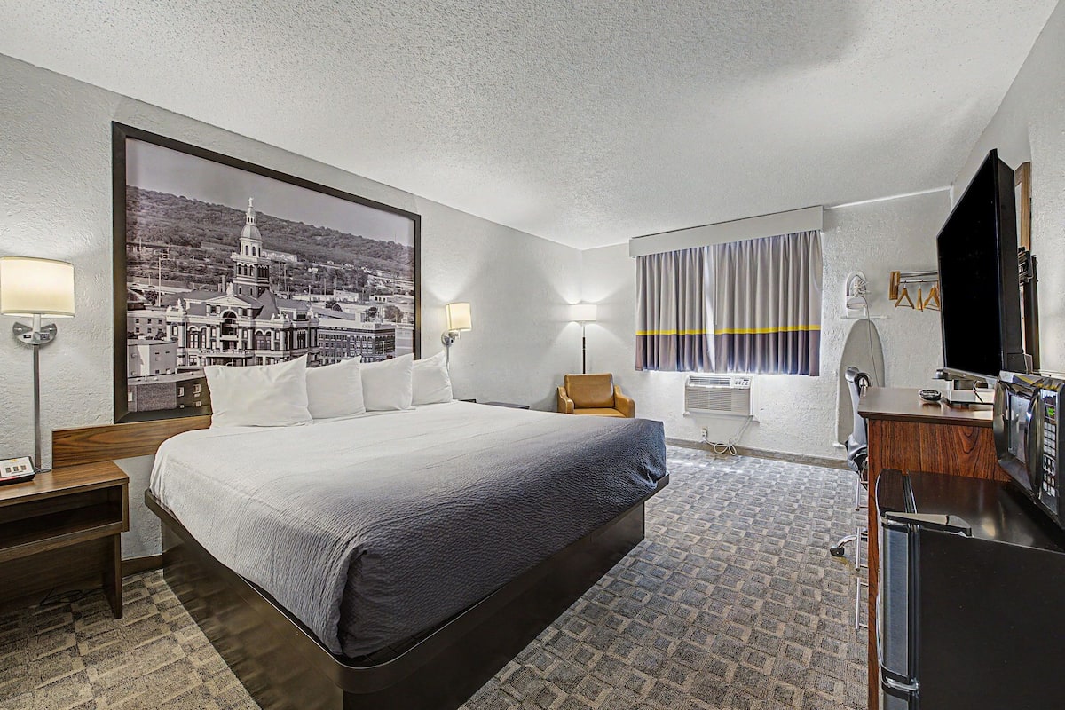 A hotel room with a large bed, a desk, a chair, a TV, and a wall-mounted air conditioner.