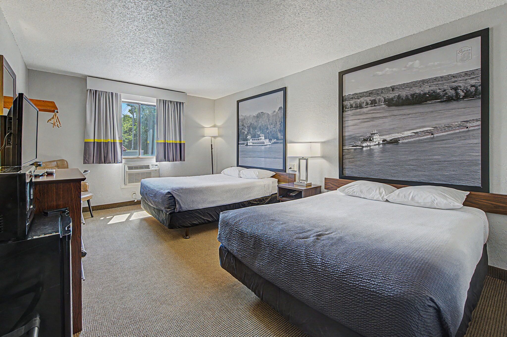 Habitación de hotel con dos camas, un escritorio, televisor y un ventanal con cortinas.