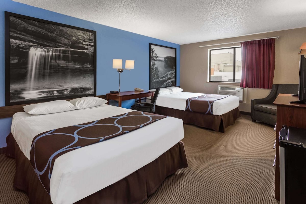 A hotel room with two beds, a desk with a lamp, a chair, a TV, and artwork on the walls.