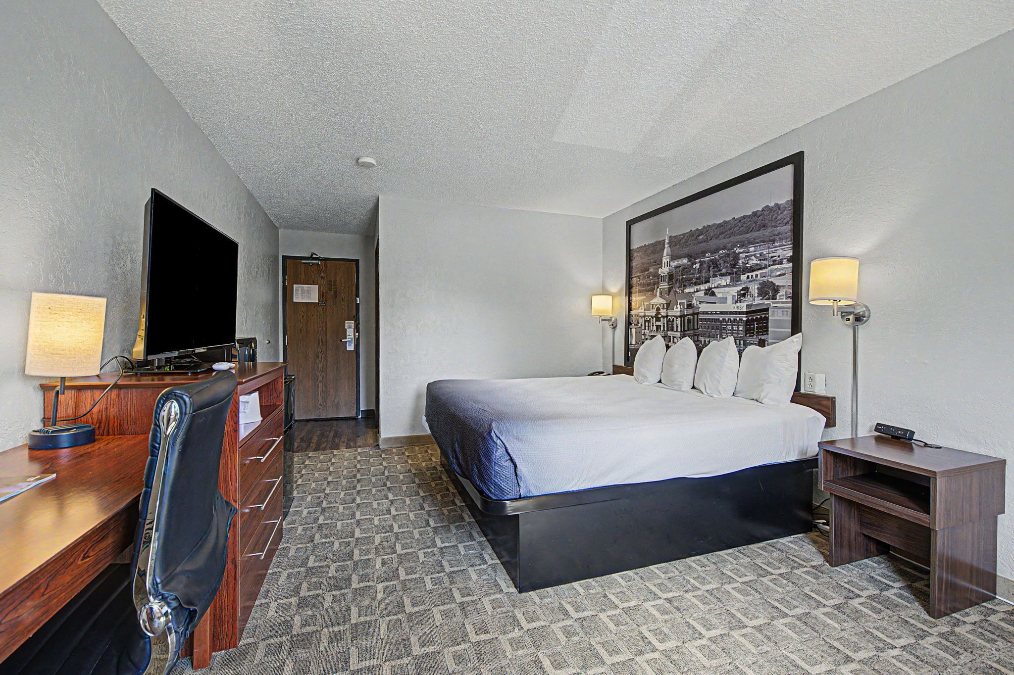 A hotel room with a bed, desk, chair, TV, and a framed picture on the wall.