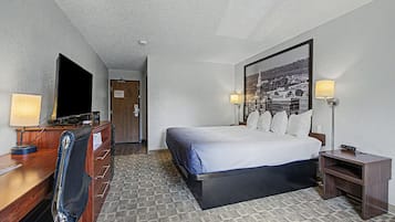 A hotel room with a bed, desk, chair, TV, and a framed picture on the wall.