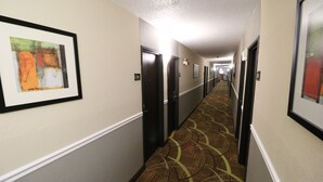 A hotel hallway with framed artwork on the walls, doors with room numbers, and patterned carpet.