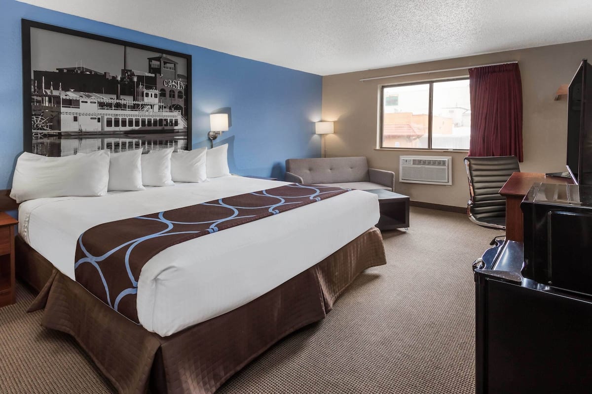 A hotel room with a large bed, a desk, a chair, a TV, and a window with curtains.