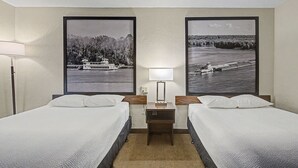 A hotel room with two beds, a nightstand with a lamp, and two large framed pictures of a river scene.