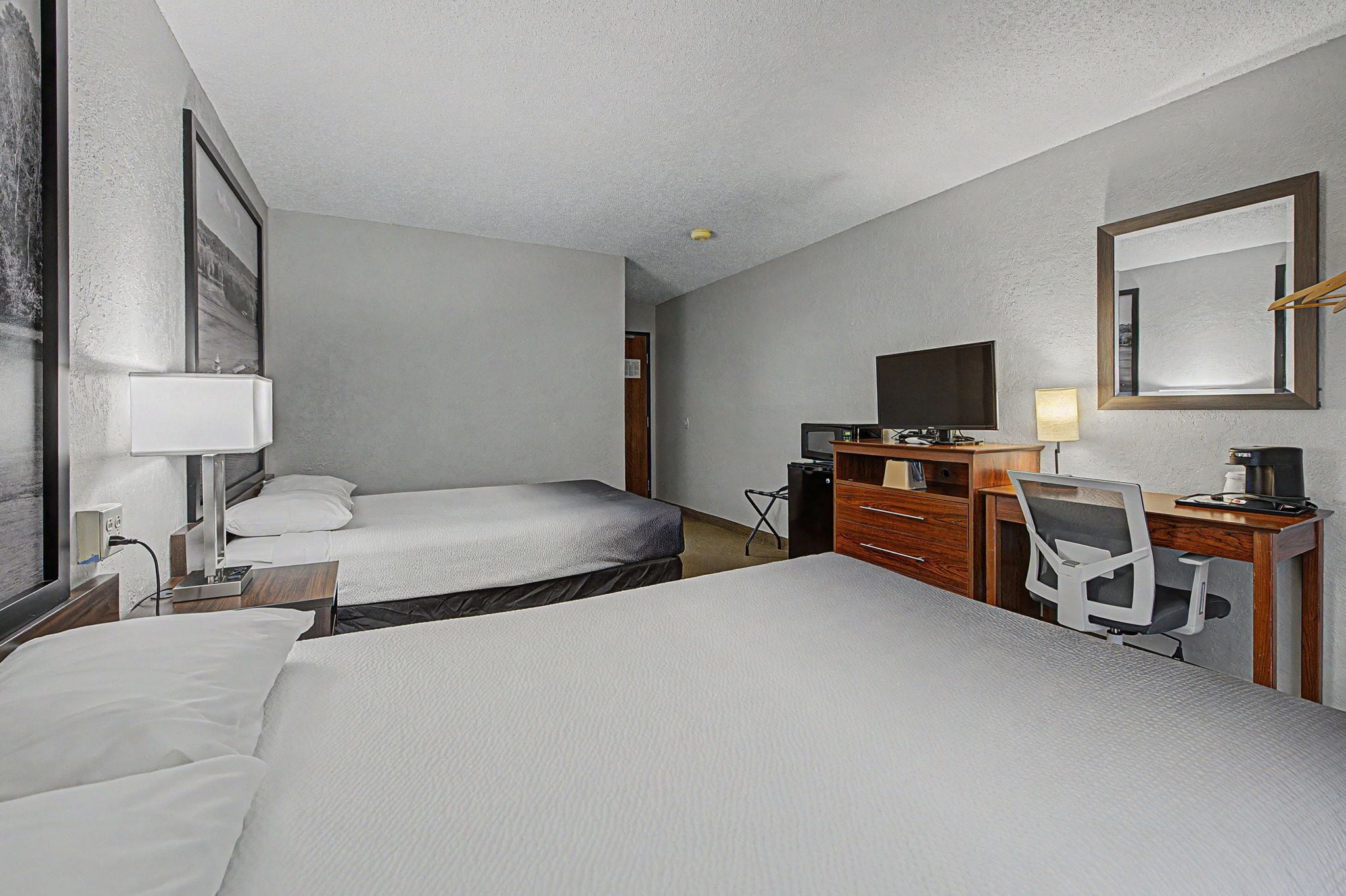 A hotel room with two beds, a desk with a chair, a television, and a mirror.