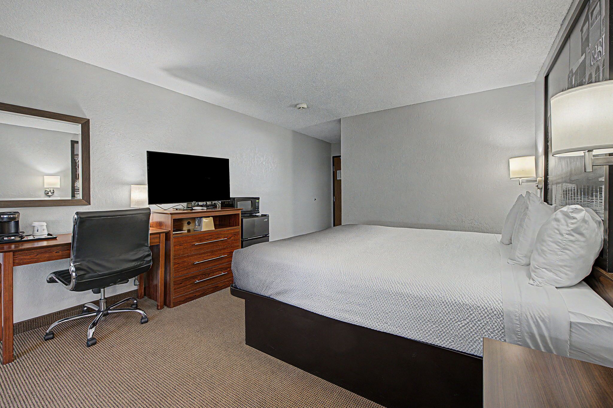 Une chambre d’hôtel comprenant un lit, un bureau avec une chaise, une télévision, une commode et une lampe.