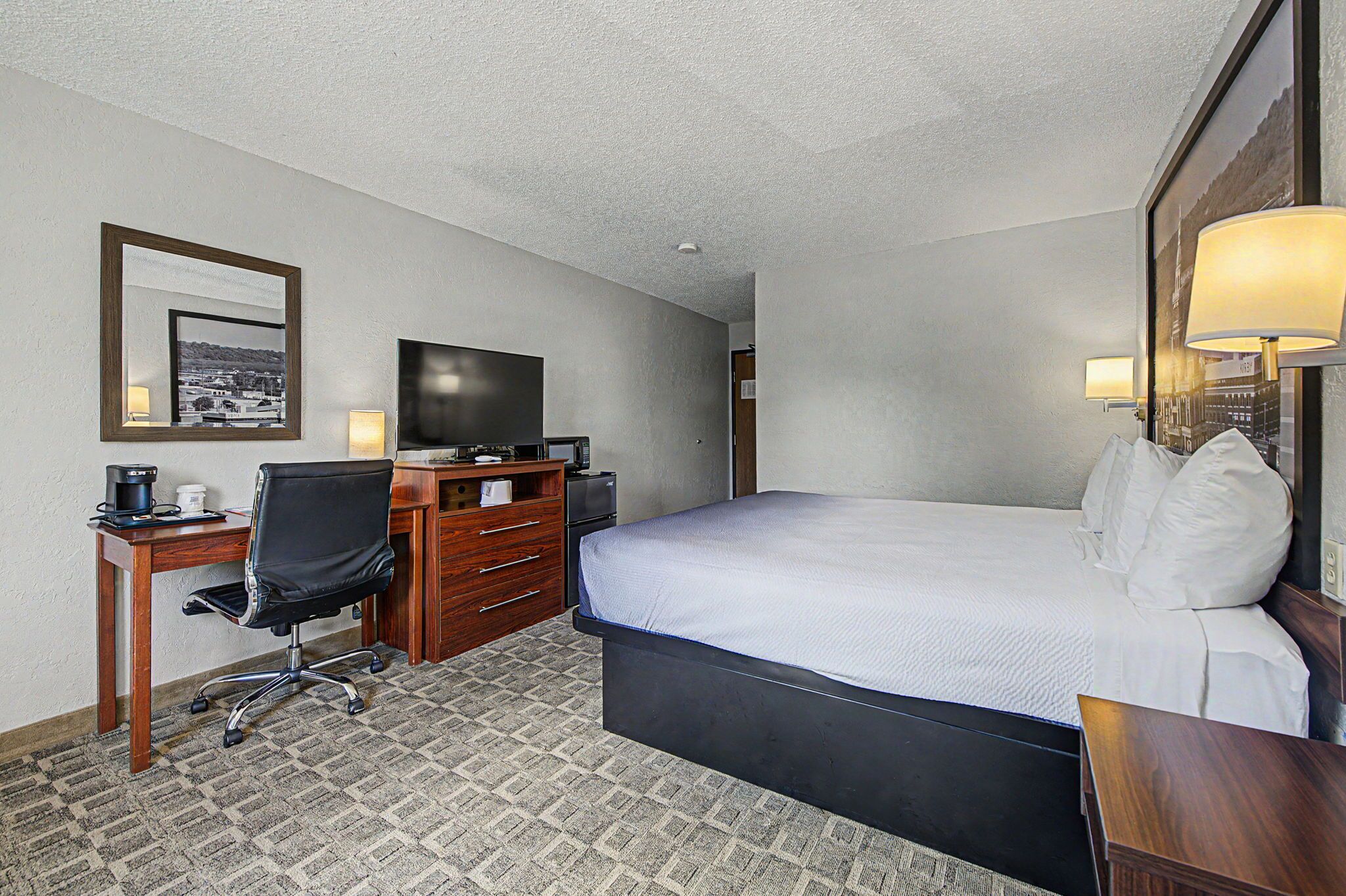 A hotel room with a bed, desk, chair, television, and lamps.