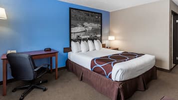 A hotel room with a bed, a desk, a chair, and a wall-mounted picture.