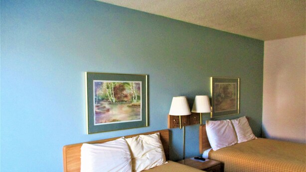 A hotel room with two beds, a nightstand, and two wall-mounted lamps. - Sunset Inn (Williamsburg)