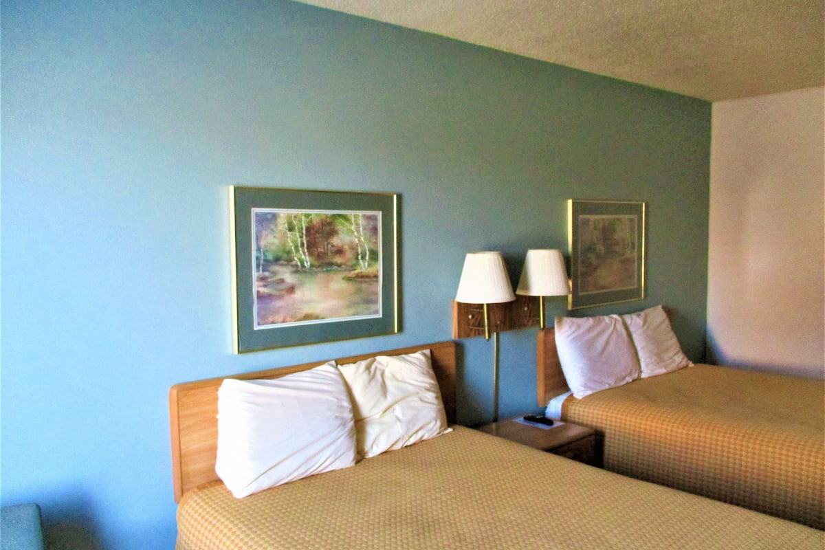 A hotel room with two beds, a nightstand, and two wall-mounted lamps.