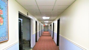 A long hallway with a patterned carpet, doors on both sides, and a ceiling with fluorescent lights. - Sunset Inn (Williamsburg)