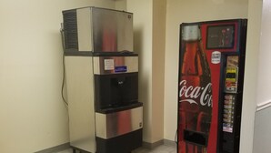 A vending machine and a refrigerator in a room with tiled flooring and plain walls. - Sunset Inn (Williamsburg)