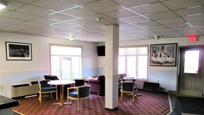 A lobby with a red carpet, a round table with chairs, a purple sofa, and a painting of swans on the wall. - Sunset Inn (Williamsburg)