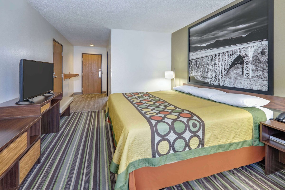 Habitación de hotel con cama, televisor, escritorio y un cuadro grande en la pared.