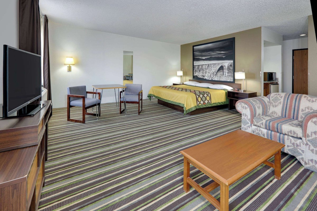 Habitación de hotel con cama, dos sillones, un sofá, un televisor y un escritorio.