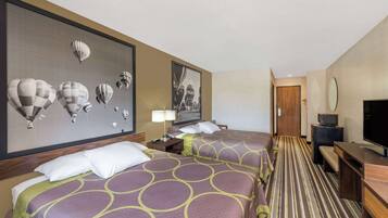 Habitación de hotel con dos camas, un televisor, un escritorio y una pared decorada con motivos de globos aerostáticos.