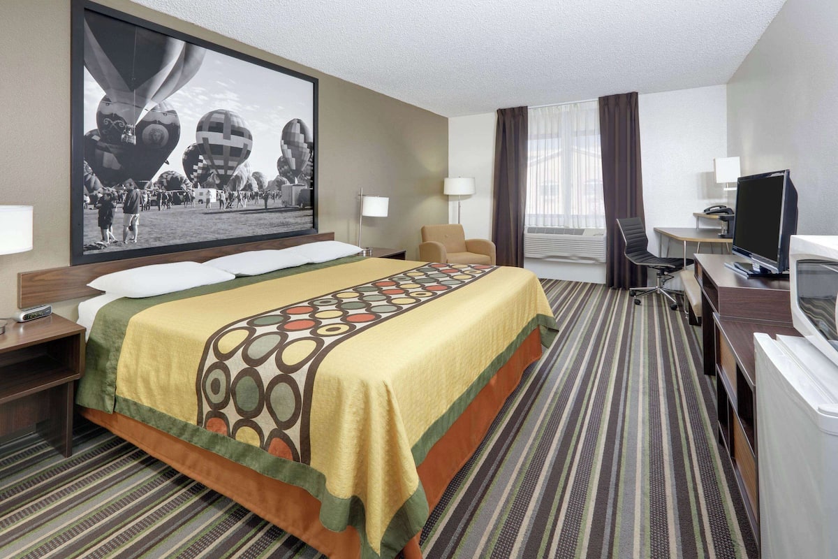Habitación de hotel con una cama grande, un escritorio con computadora, un televisor y un cuadro grande en la pared.