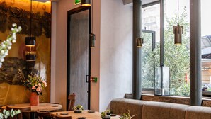Interior de restaurante con mesas y sillas de madera, lámparas colgantes y un ventanal con vistas al exterior.
