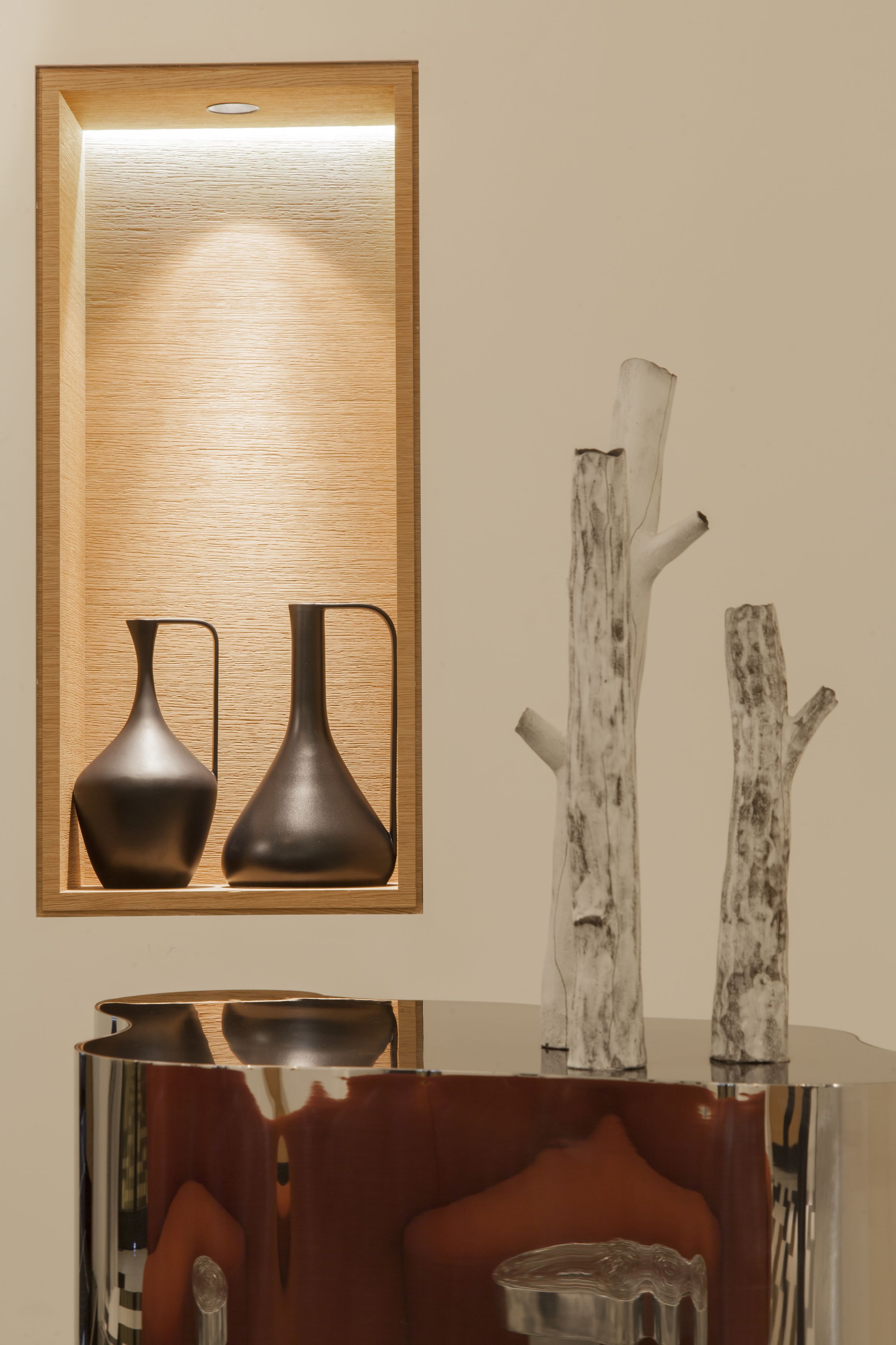 Un interior moderno con un espejo de madera, dos jarrones oscuros y dos troncos de árbol blancos sobre una superficie reflectante.