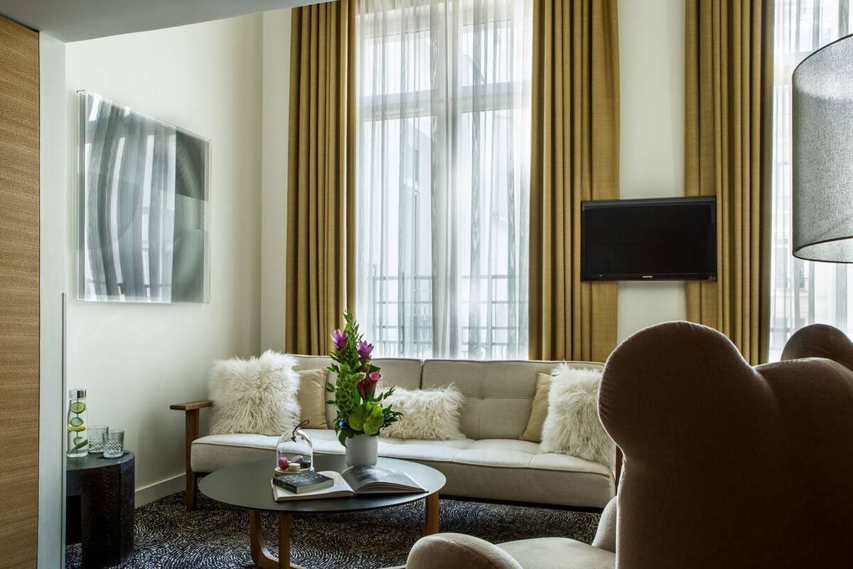 Una sala moderna con un sofá, una mesa de centro, un televisor y un ventanal con cortinas.