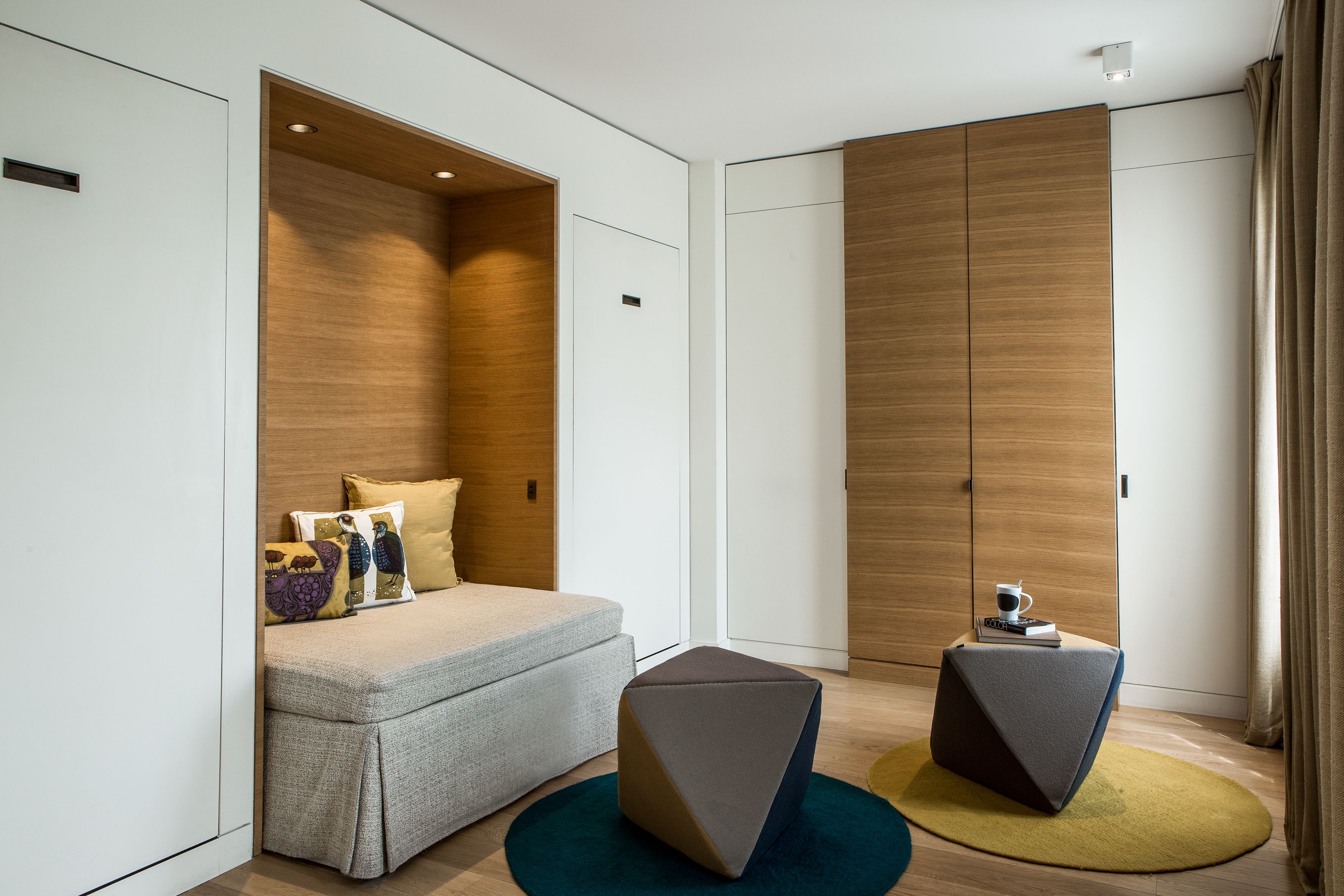 A modern hotel room with a sofa, two ottomans, a coffee table, and a wardrobe.
