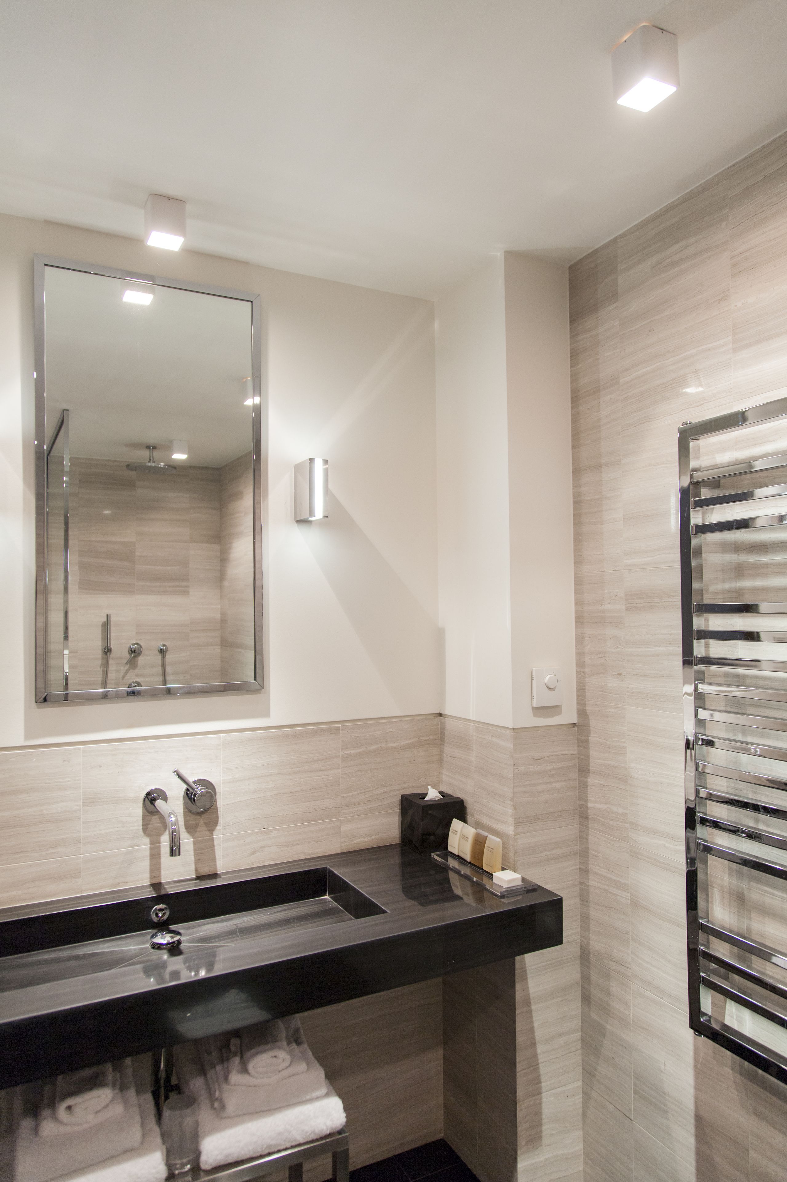 A modern bathroom with a black sink, a large mirror, a towel rack, and a shower area.
