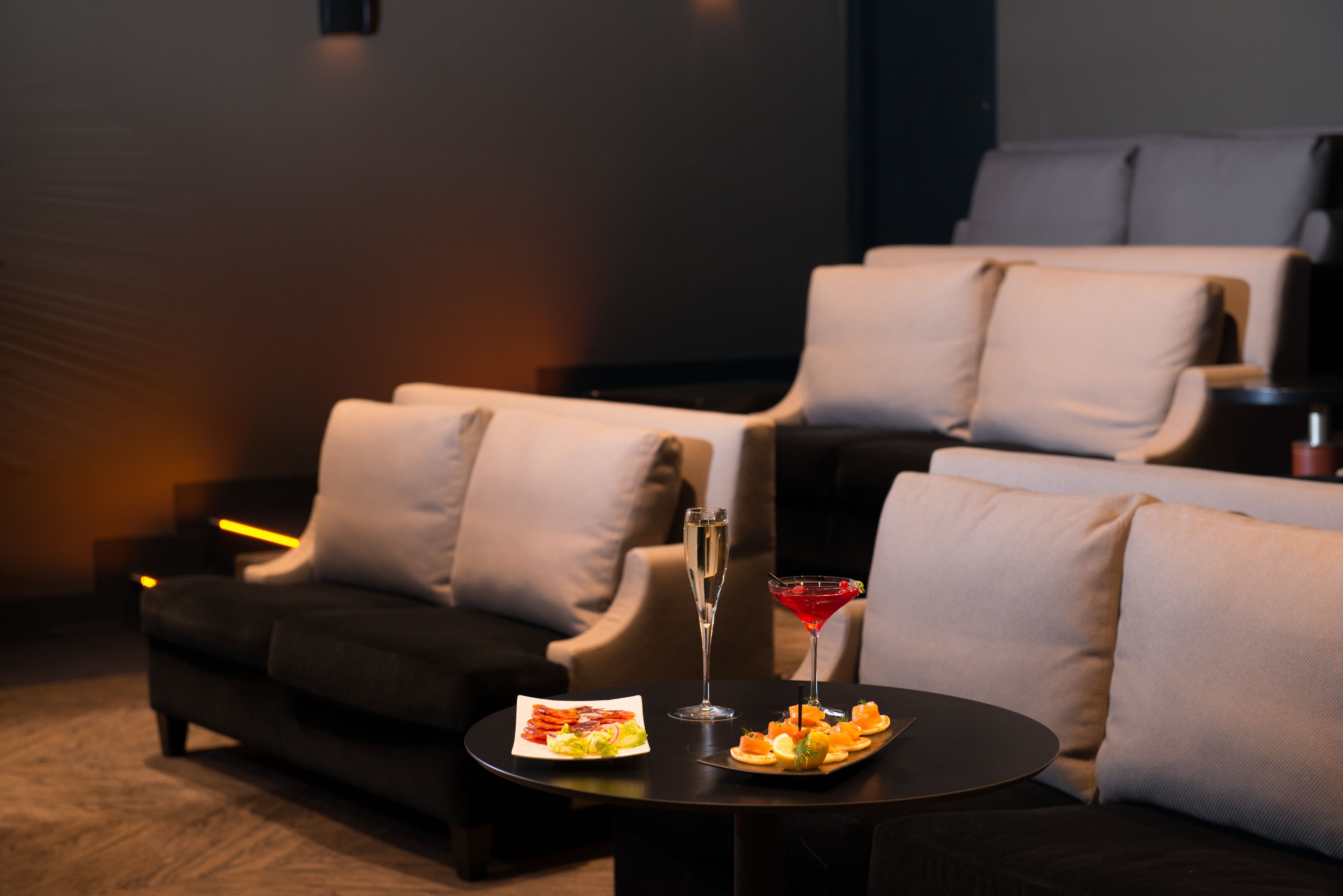 A cozy seating area with a sofa and armchairs, a small table with snacks and drinks, and a bar area in the background.