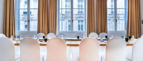 A conference room with a long table, white chairs, and large windows with curtains.
