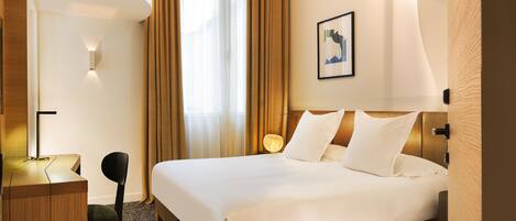A hotel room with a bed, desk, chair, and a painting on the wall.