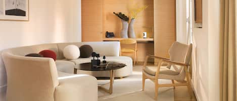 A modern living room with a sofa, armchairs, a coffee table, and a side table. There is a wooden cabinet in the background and a framed picture on the wall.