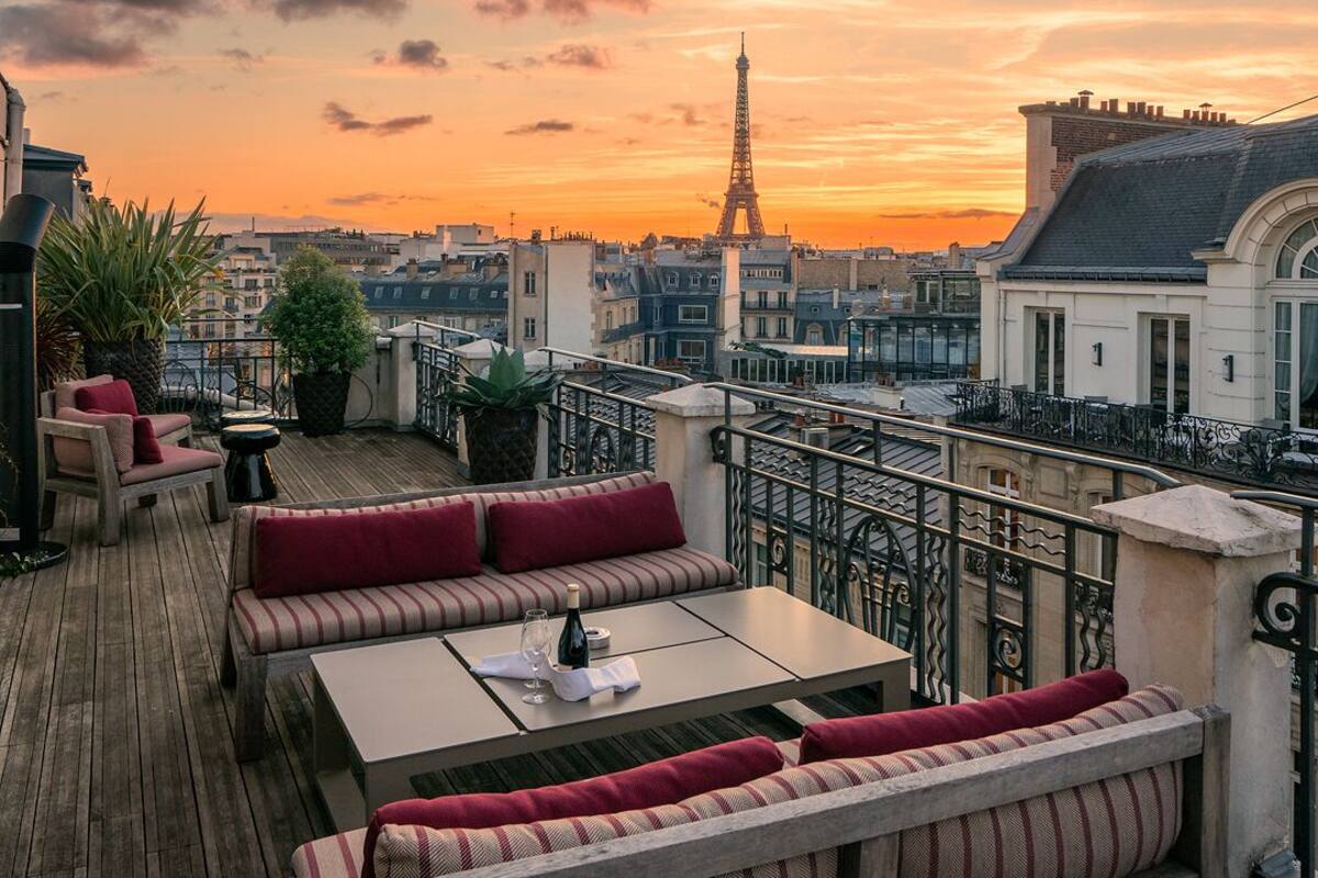 Una terraza en la azotea con suelo de madera, zonas de estar y vistas al Torre Eiffel al atardecer.