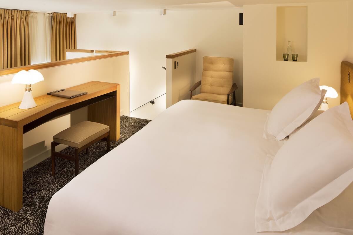 Una habitación de hotel con una cama, un escritorio con una silla, un espejo y una lámpara.