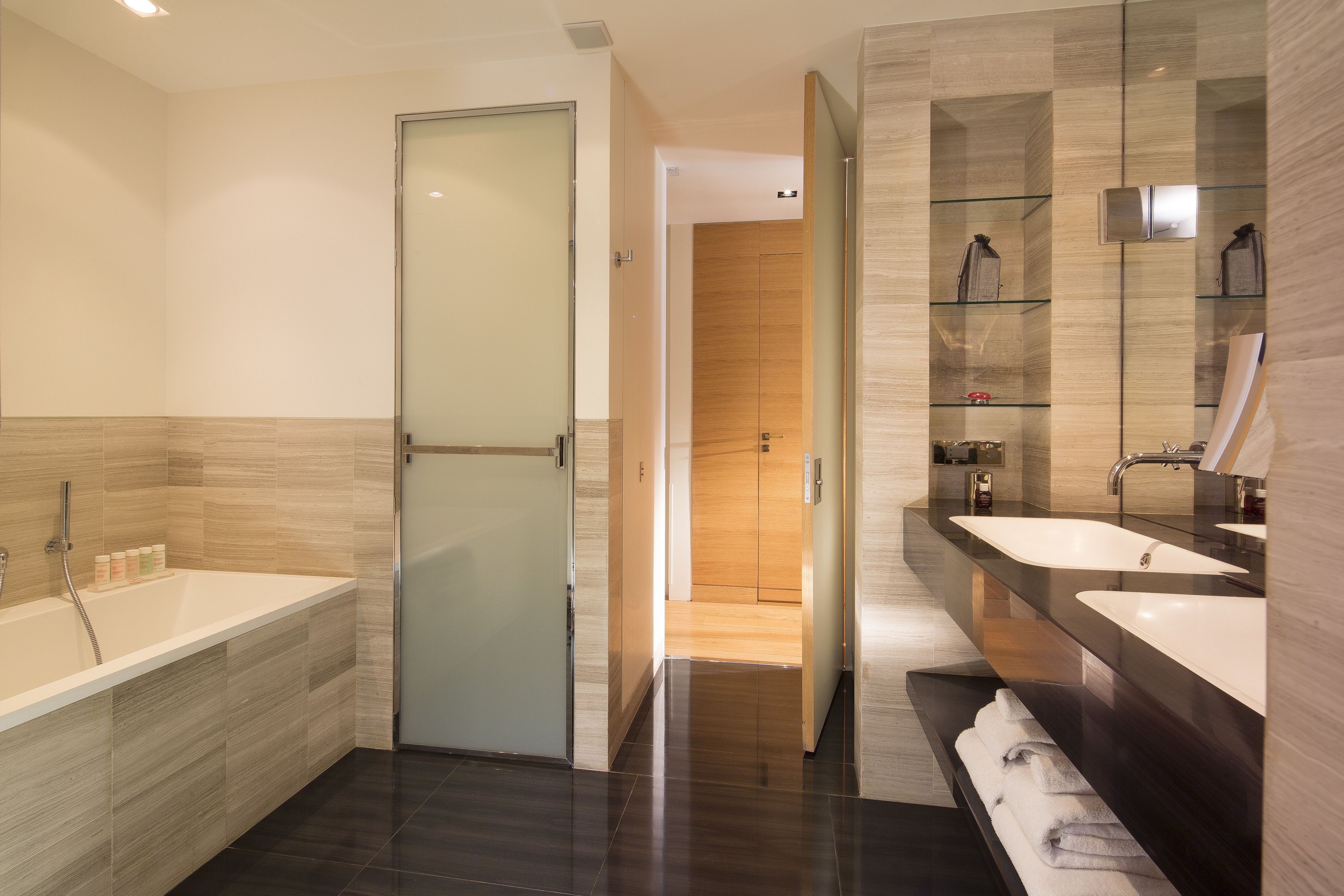 A modern bathroom with a bathtub, two sinks, a glass shower enclosure, and a wooden vanity.