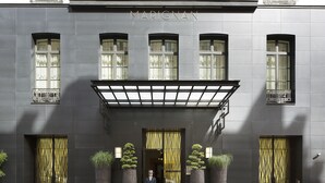 Fachada de un edificio con el nombre "MARIGNAN" sobre la entrada, ventanas grandes con cortinas y un hombre de pie frente a él.
