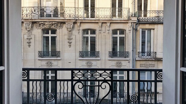 Un balcón con una bandeja de desayuno, una cama y vistas a un edificio clásico con balcones ornamentados.