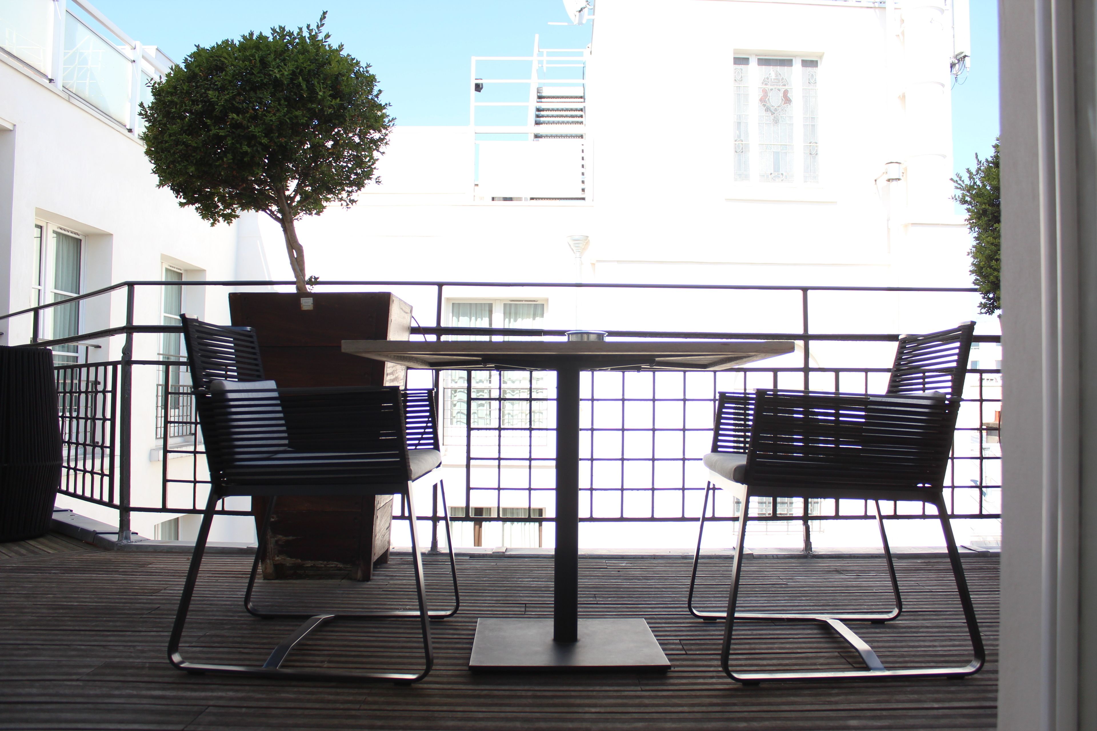 A balcony with a table and two chairs, a potted tree, and a view of buildings.