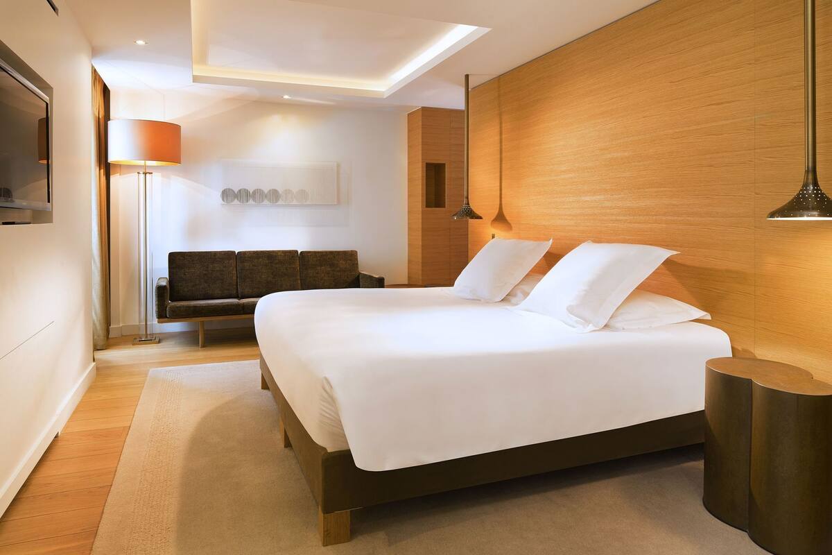 Un dormitorio moderno con una cama grande, un sofá, un televisor y una pared de acento de madera.