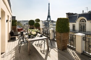 Una terraza en la azotea con una mesa, sillas, plantas en macetas y vistas de la Torre Eiffel.