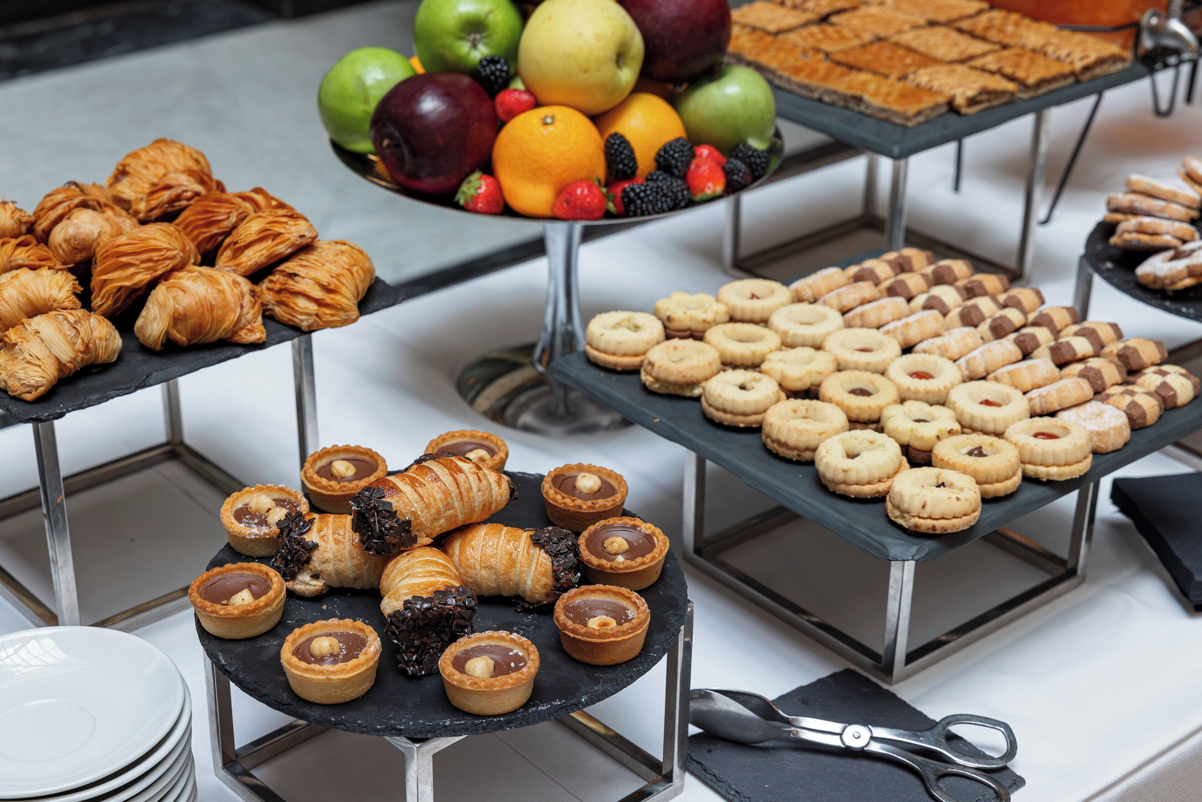 A buffet table with various pastries, tarts, and a selection of fruits.