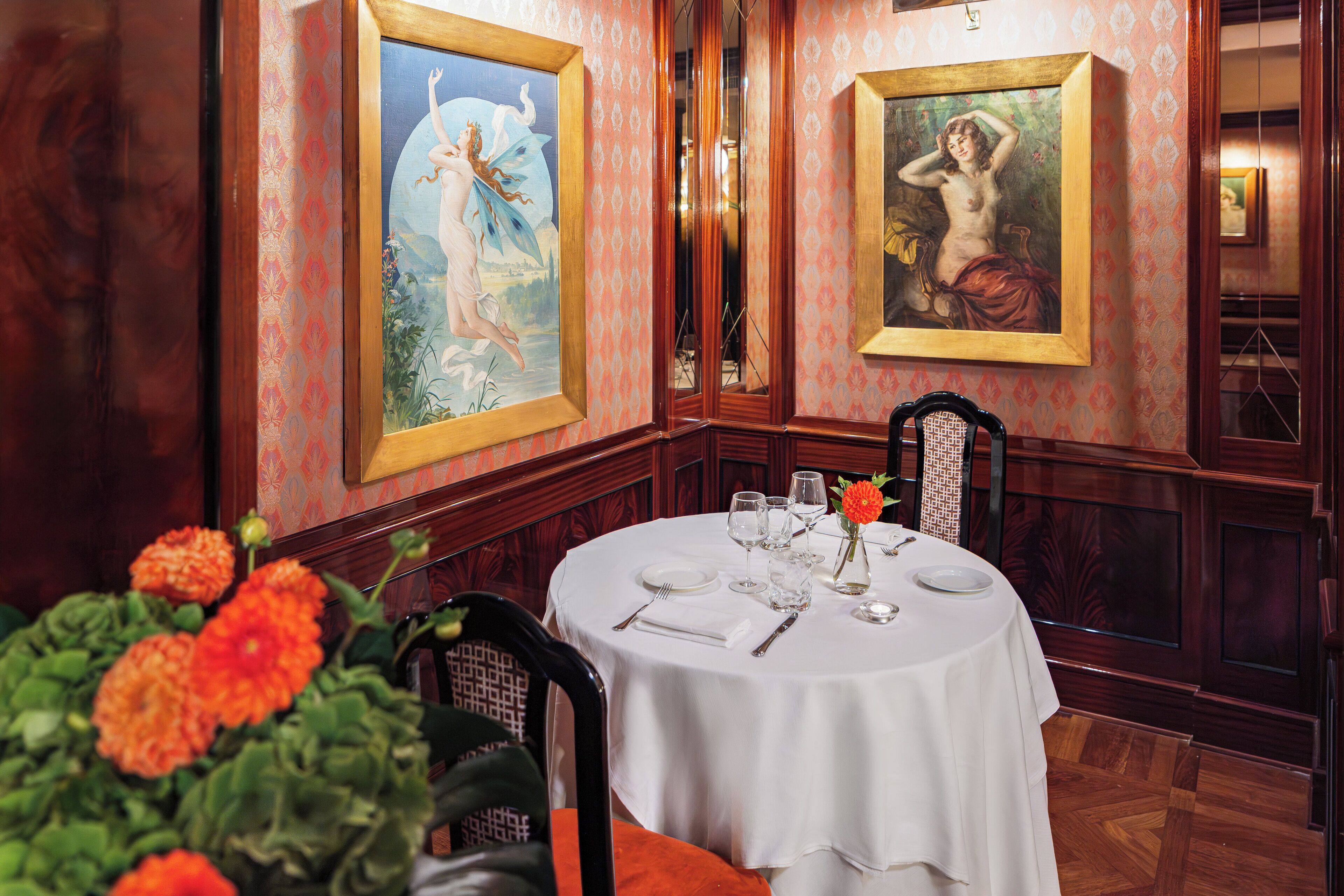 A dining area with a round table set for four, surrounded by chairs, with artwork on the walls and a vase of flowers on the table.