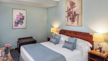 Una camera d'albergo ordinata con un letto grande, due comodini con lampade e due quadri floreali appesi alle pareti.