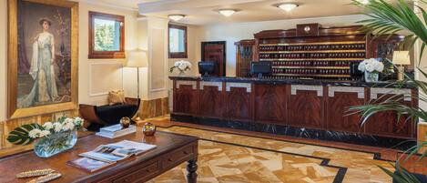 A lobby with a reception desk, a large painting, a bookshelf, and a patterned floor.