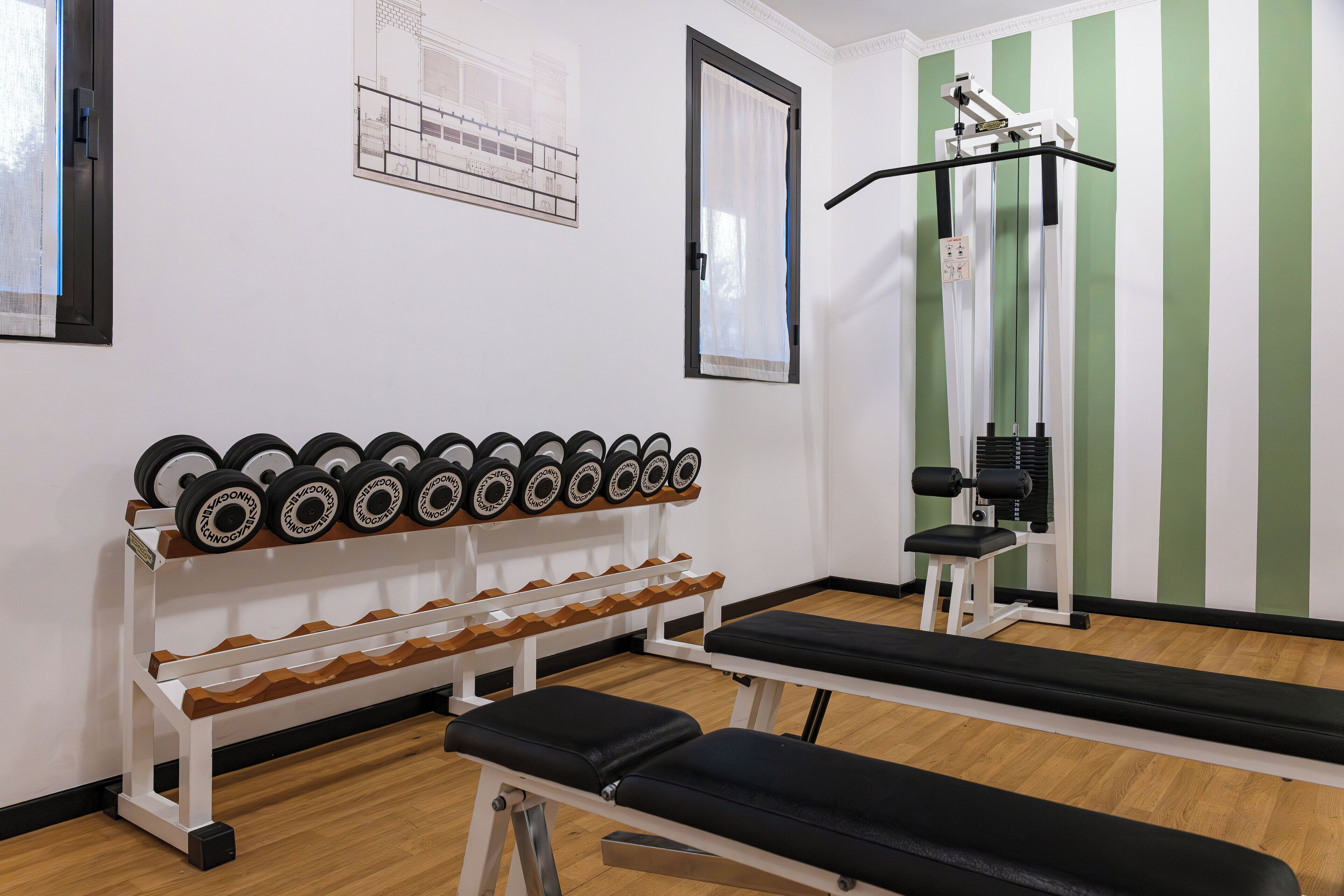 Un gimnasio con equipo de levantamiento de pesas, bancos y una jaula para sentadillas.