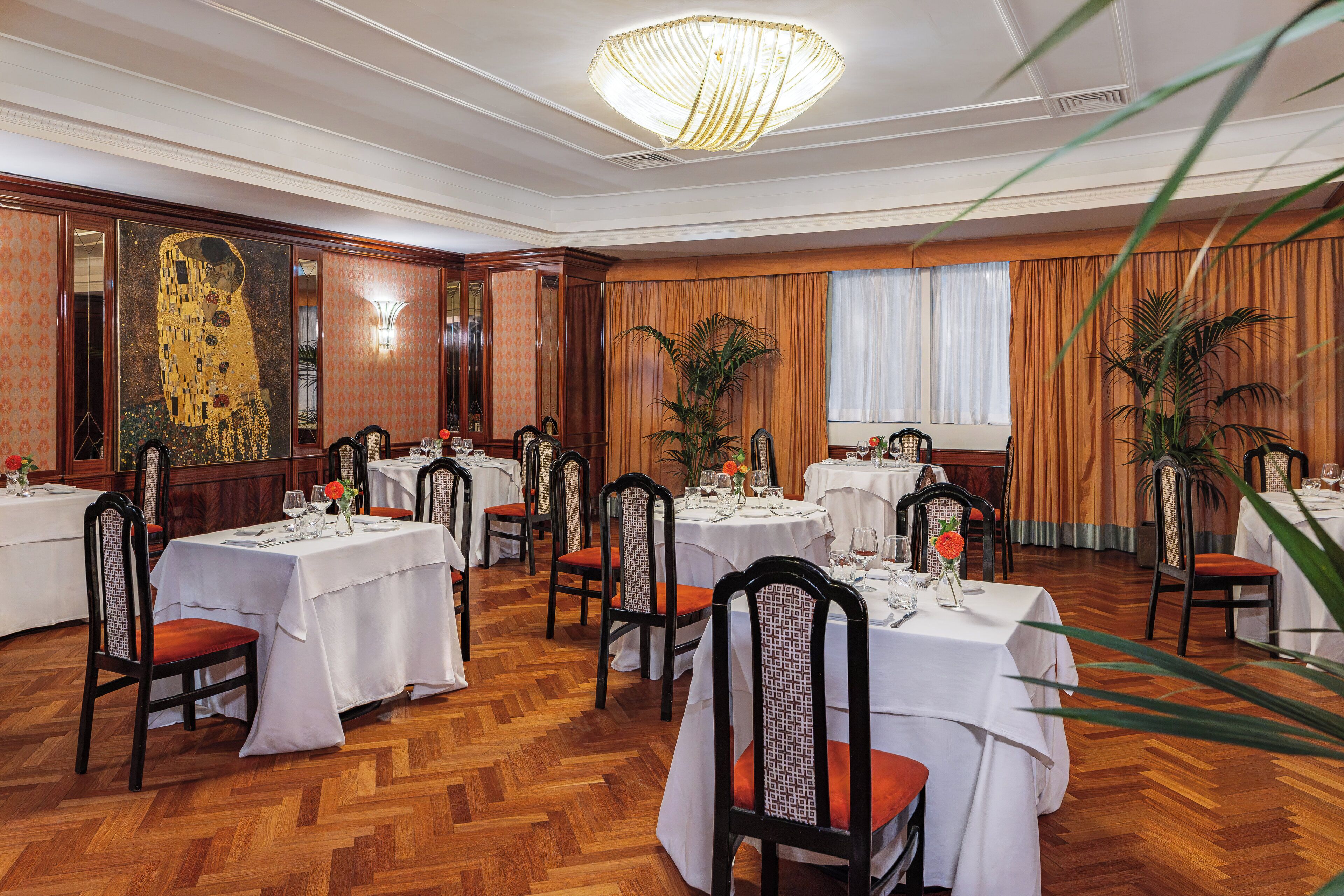 Un comedor con mesas redondas, sillas y un cuadro grande en la pared.