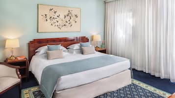 Ein Hotelzimmer mit einem großen Bett, zwei Nachttischen mit Lampen, einem Sessel, einer Wanddekoration und einem großen Fenster mit Vorhängen.
