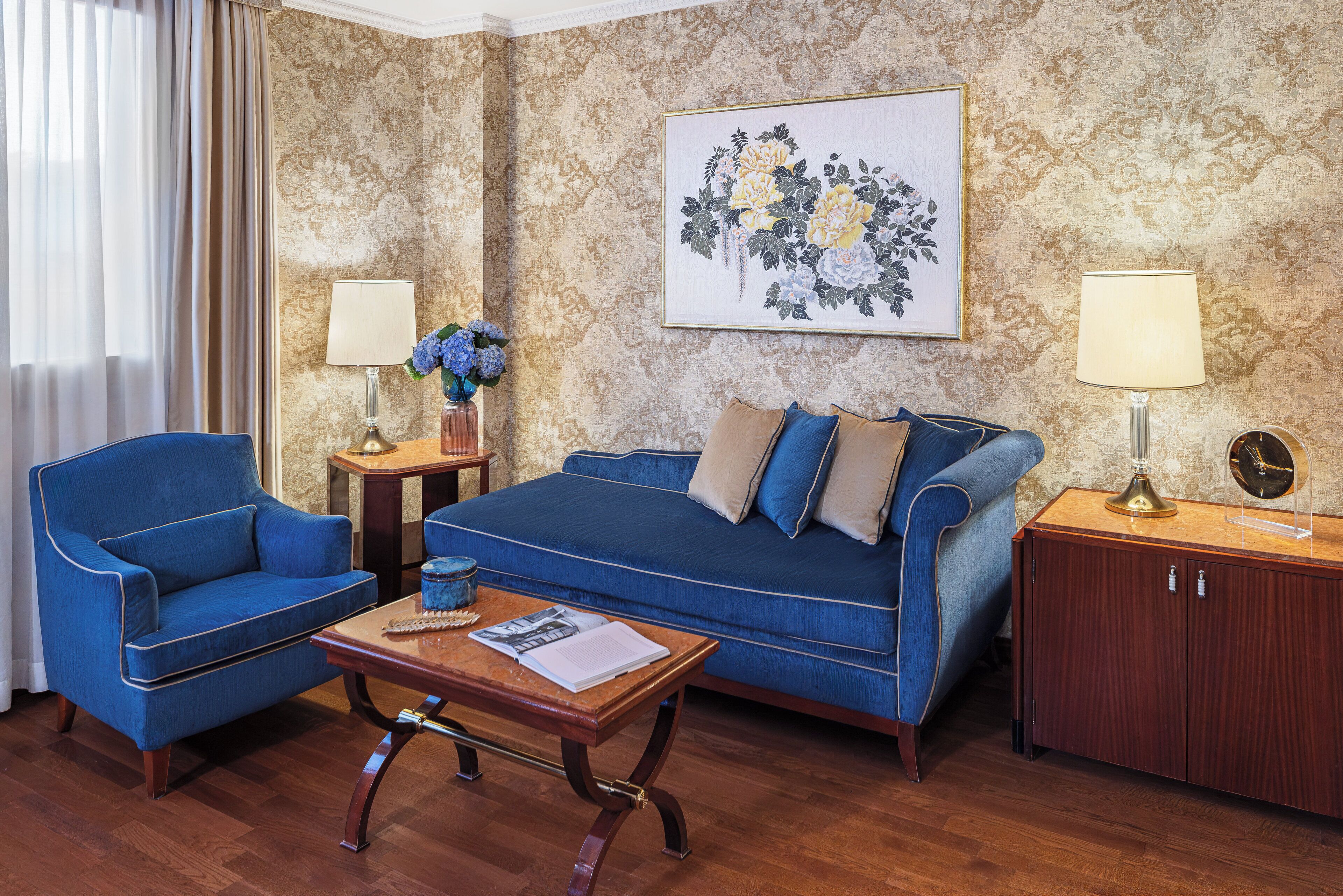 A living room with a blue sofa, matching armchair, wooden coffee table, and a cabinet with a lamp.