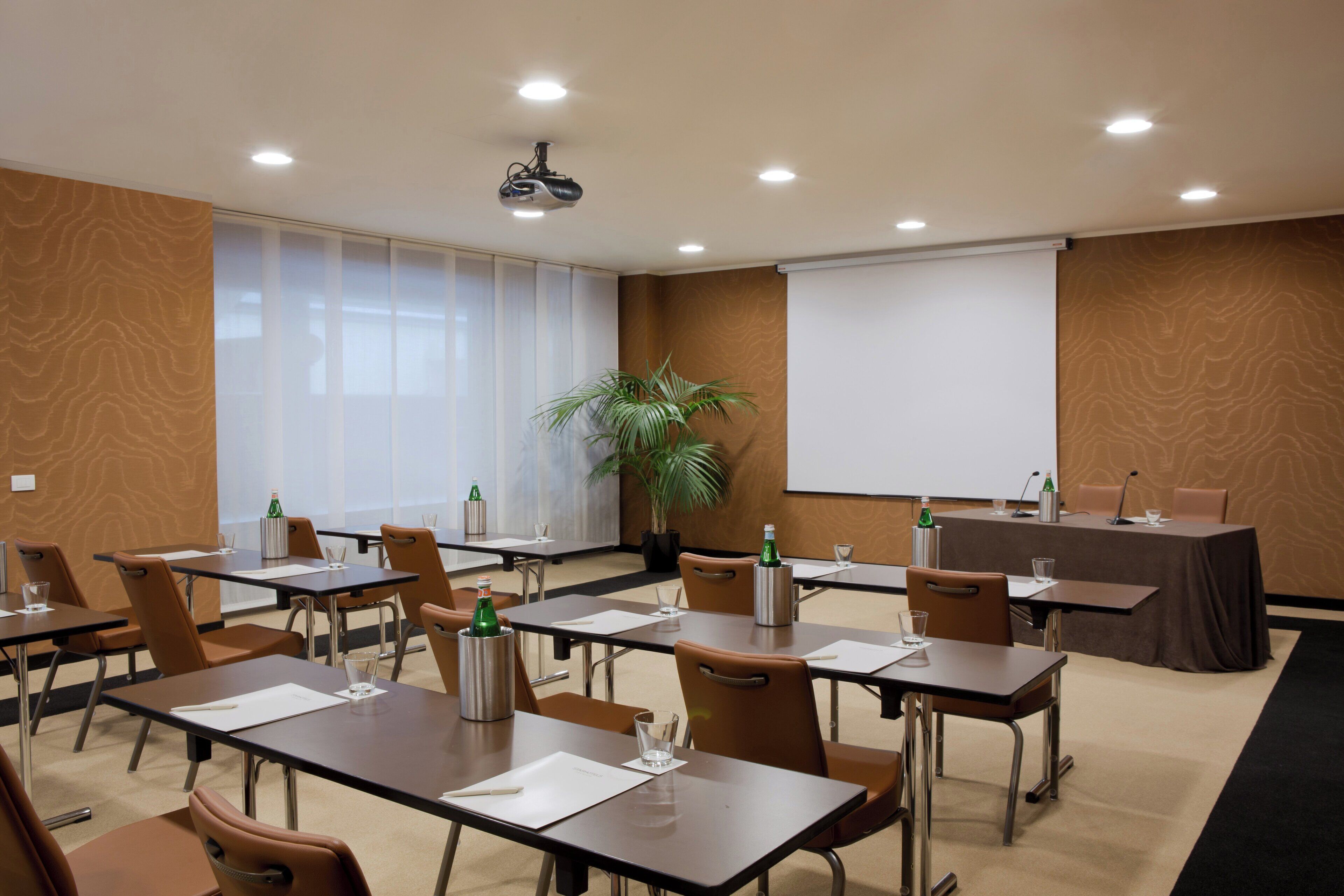 A conference room with tables, chairs, a projector, and a screen.